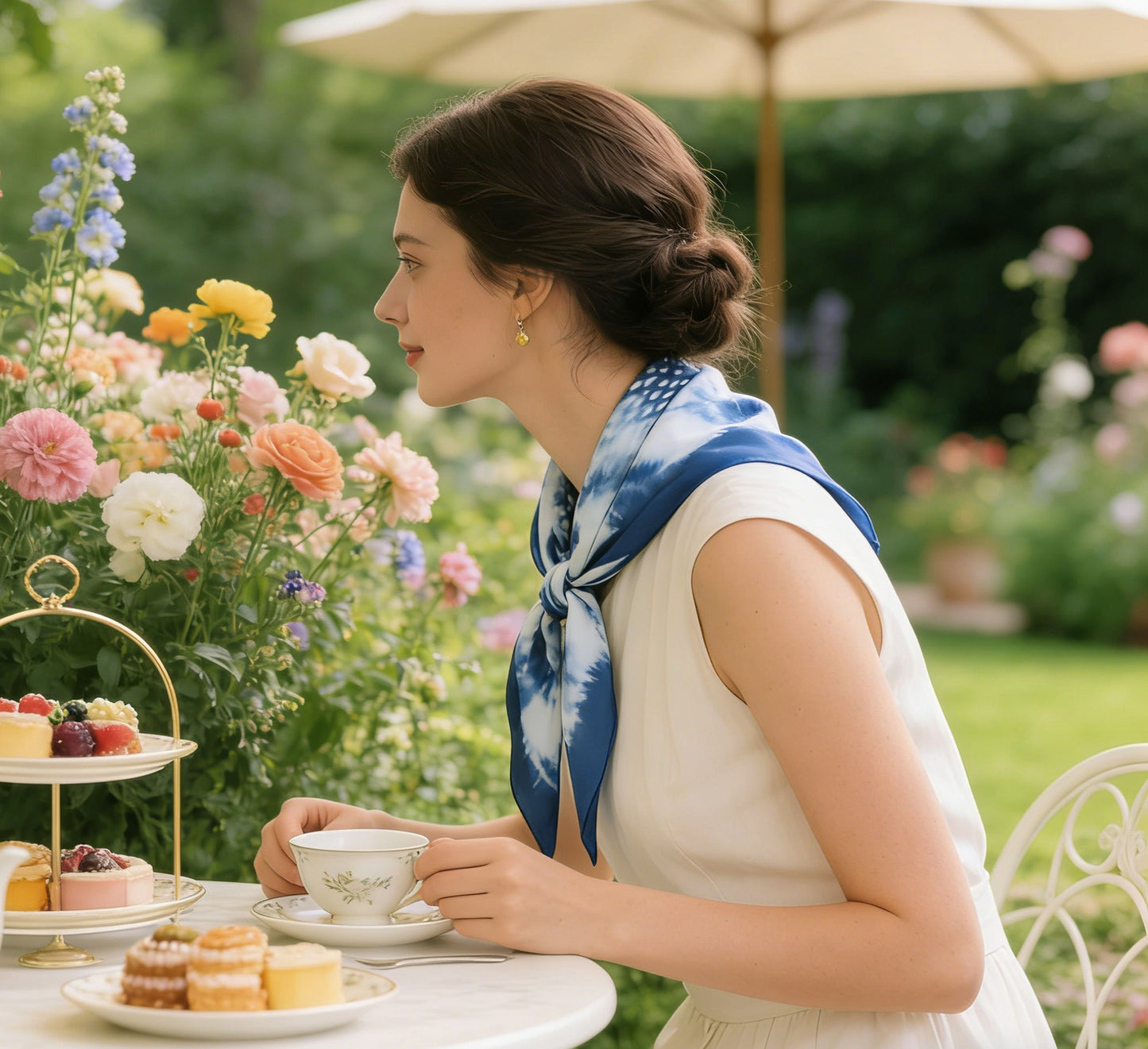 Woman enjoying tea outdoors with a floral arrangement and pastries.