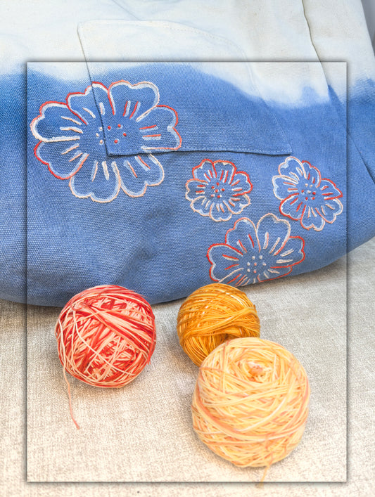 Blue fabric with floral patterns and three balls of yarn on a textured surface