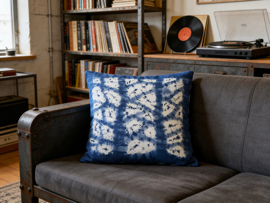 Blue and white patterned pillow on a gray sofa with a bookshelf and record player in the background.