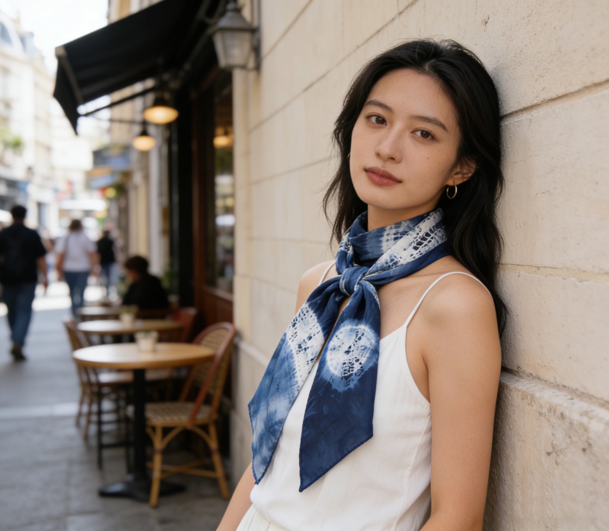 Woman wearing a blue patterned scarf leaning against a wall in an urban setting.