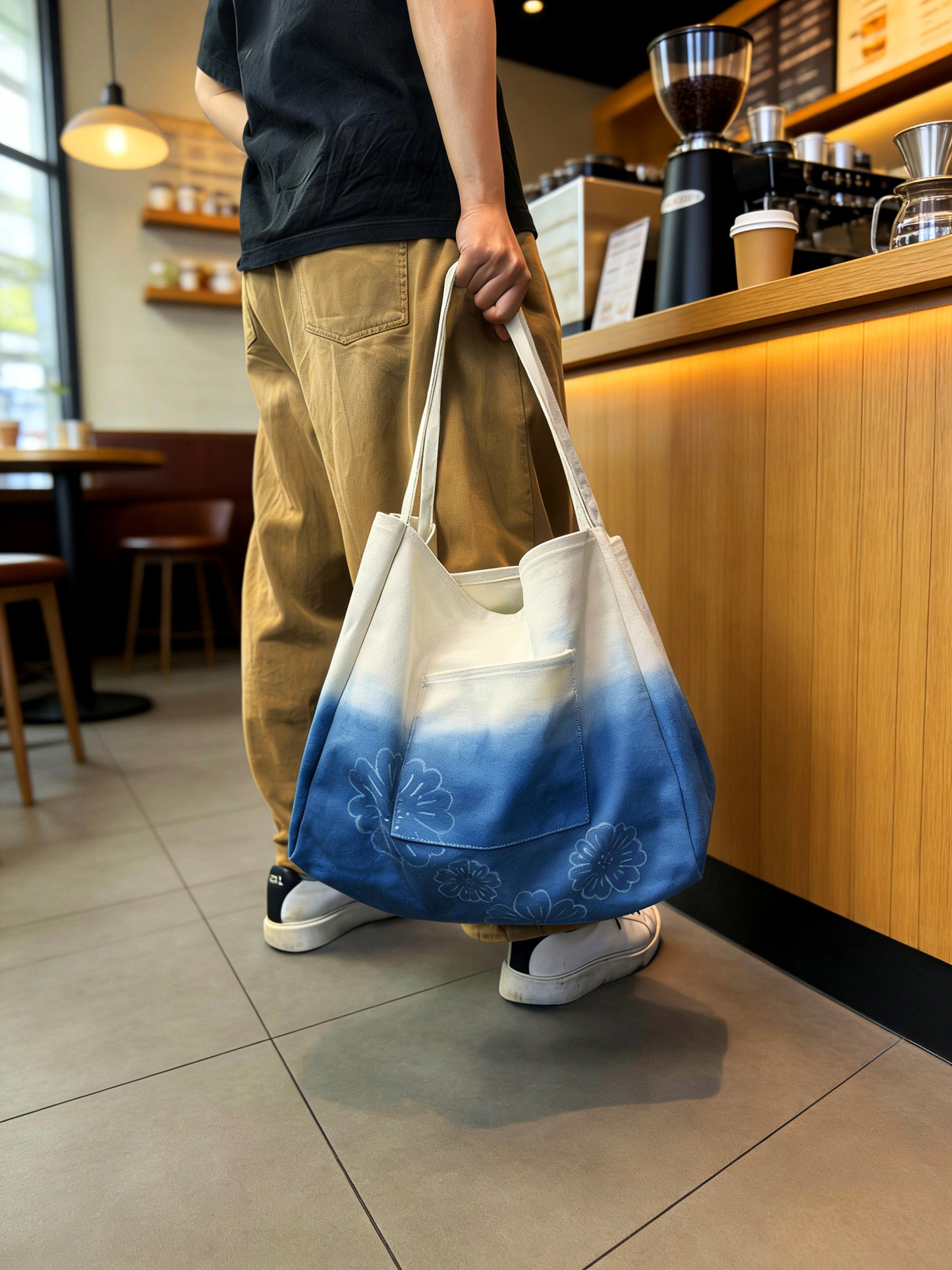 Person holding a blue and white gradient tote bag in a coffee shop.