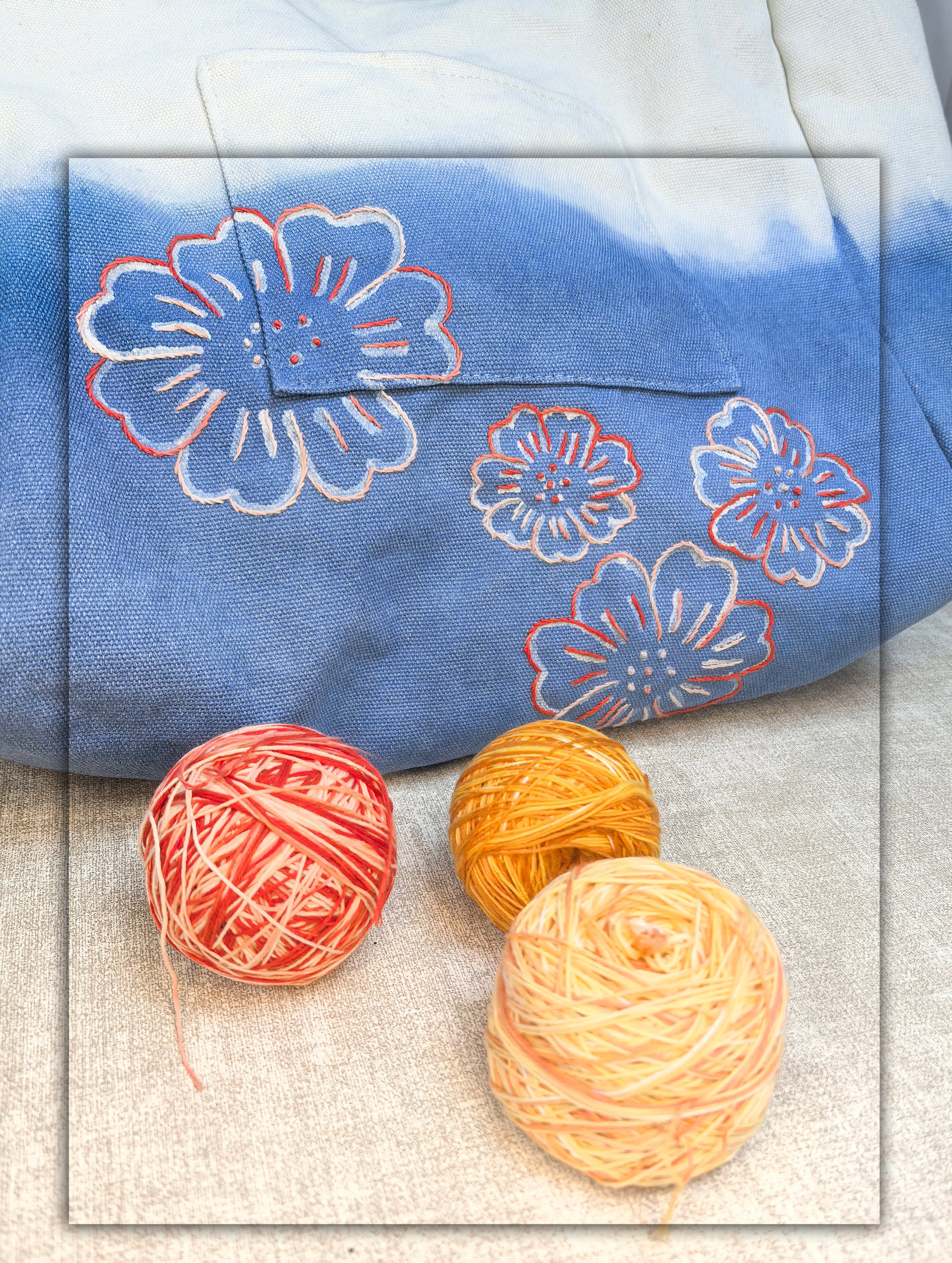 Blue fabric with floral patterns and three balls of yarn on a textured surface