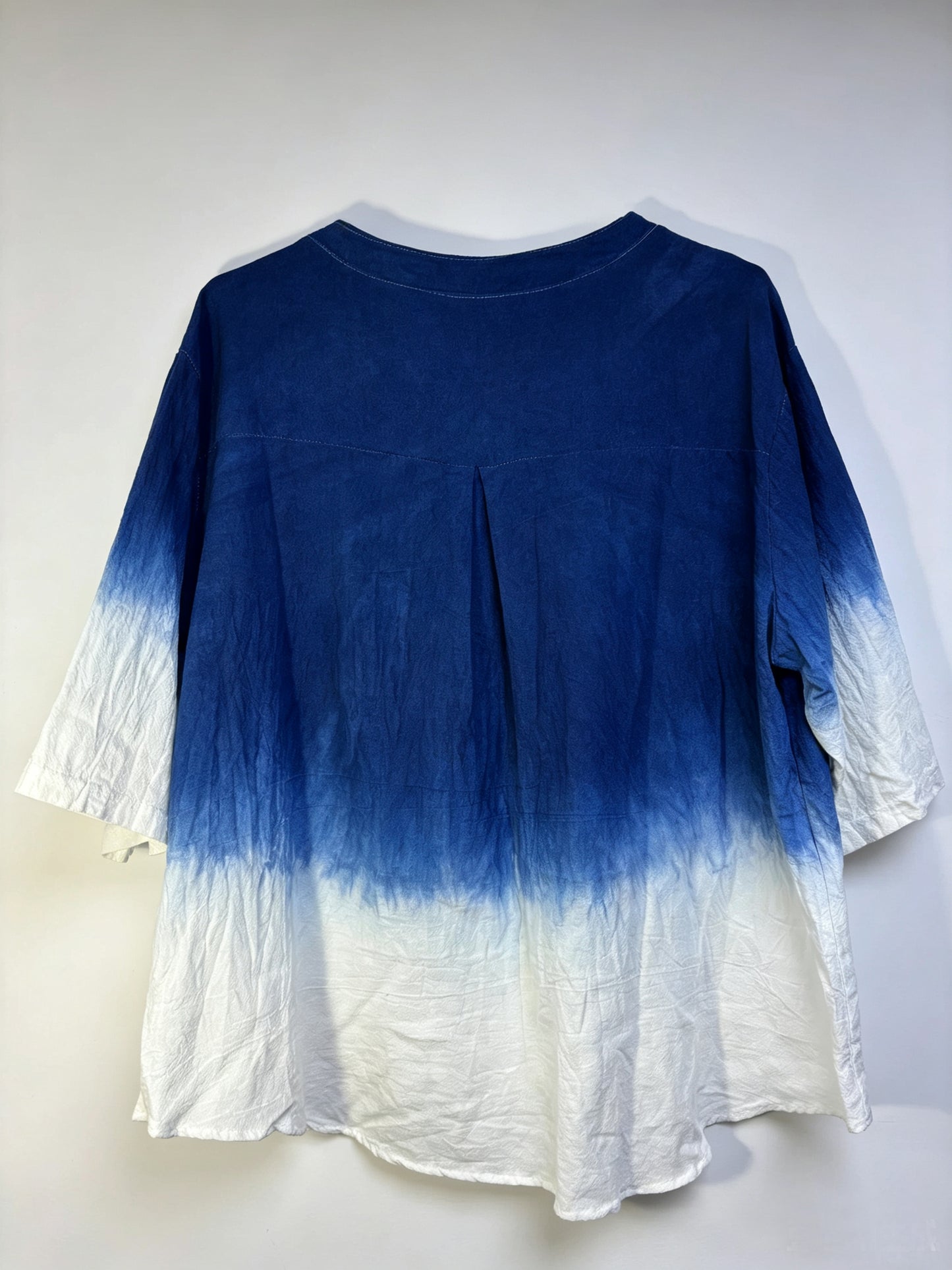 A blue and white tie-dye blouse with a crew neck and elbow-length sleeves, shown hanging against a plain light background.