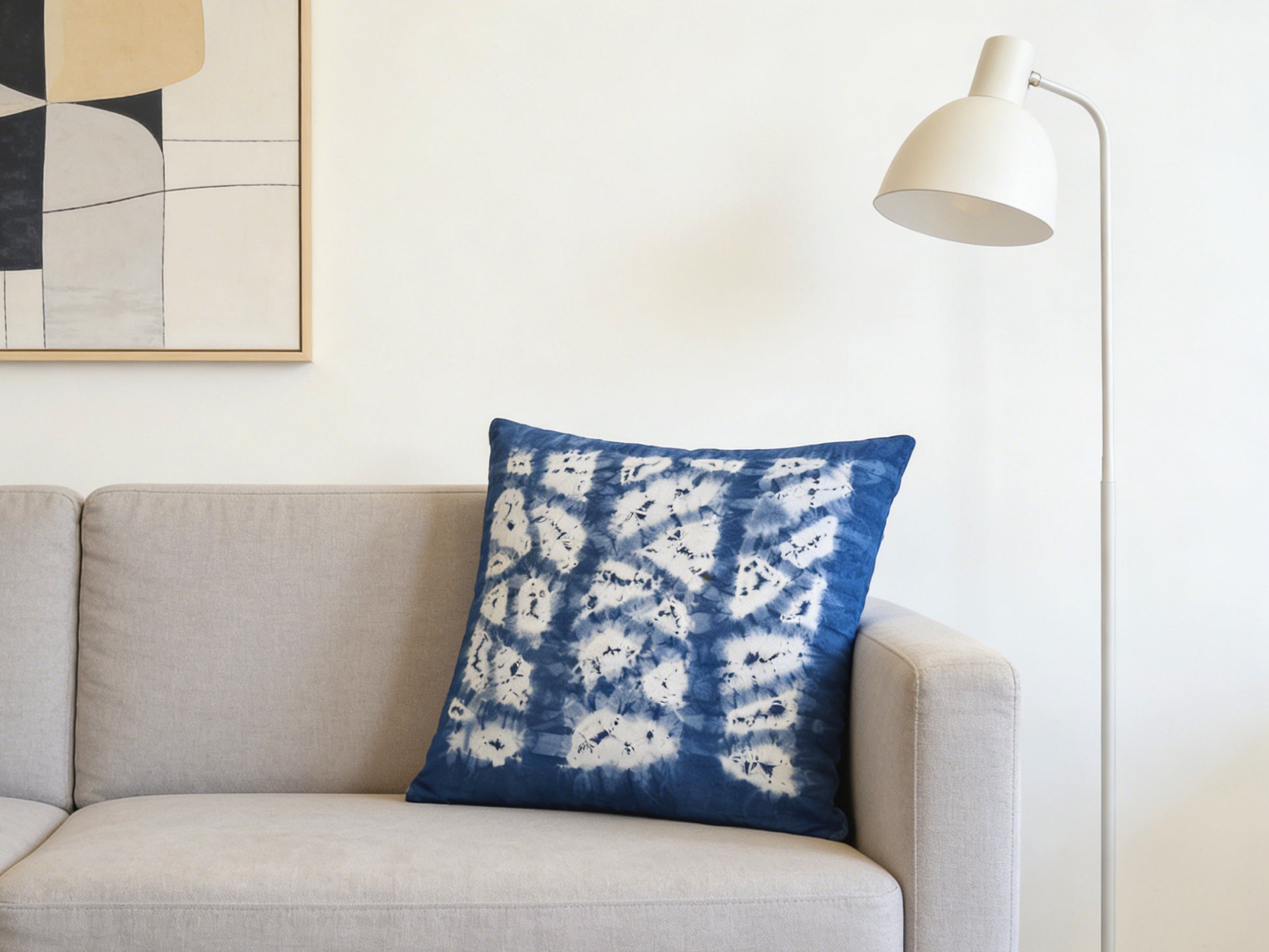 Blue and white patterned pillow on a gray sofa with a lamp and abstract art in the background.