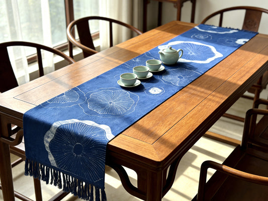 Wooden dining table with a blue table runner featuring white floral patterns, accompanied by teacups and a teapot.