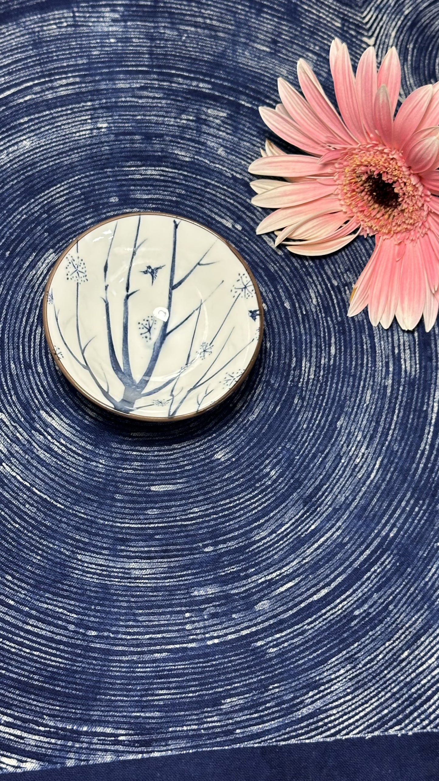 Round ceramic object with floral design on a textured blue surface with a pink flower.