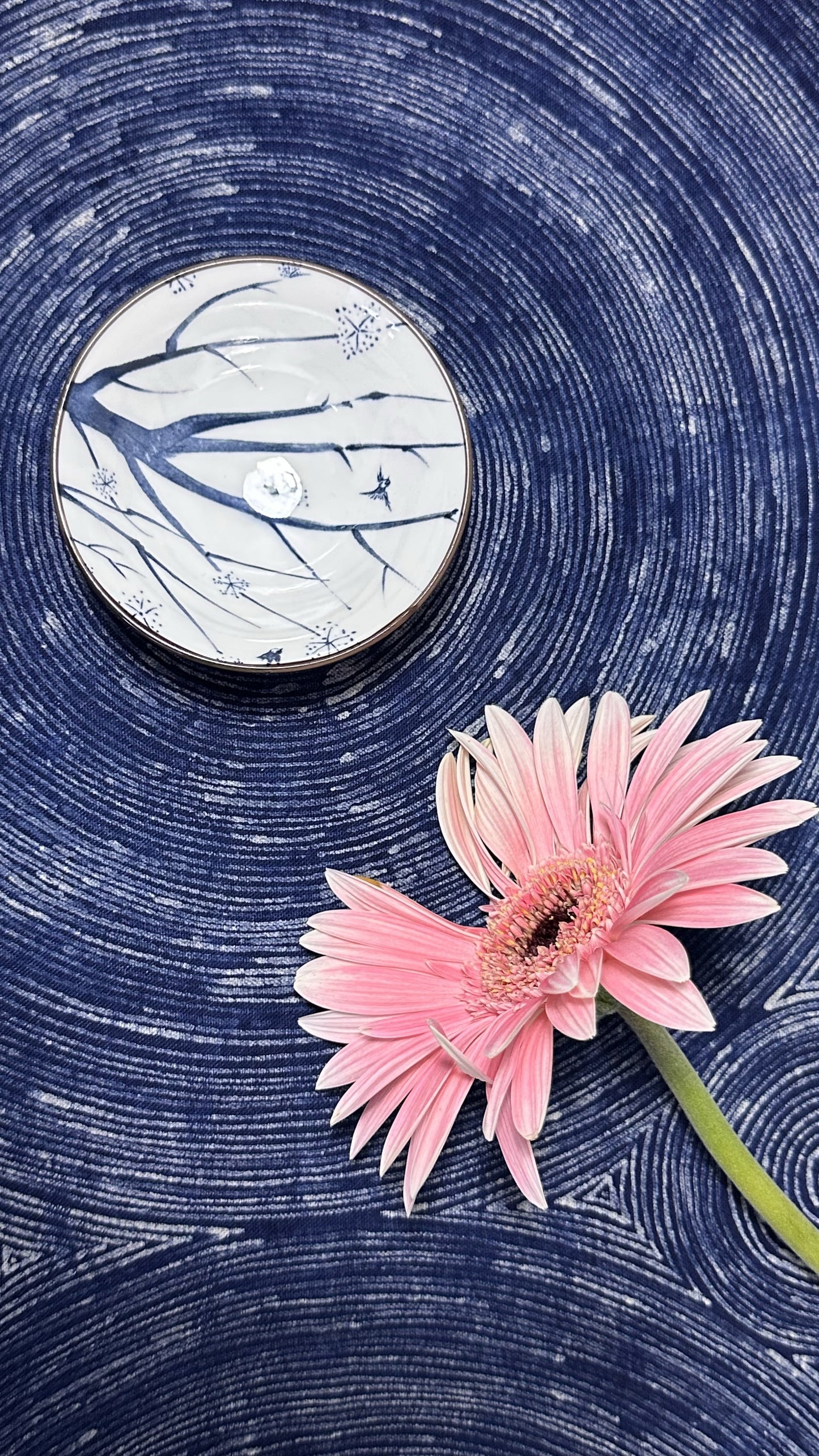 Pink flower on a blue textured surface with a circular object featuring abstract designs.
