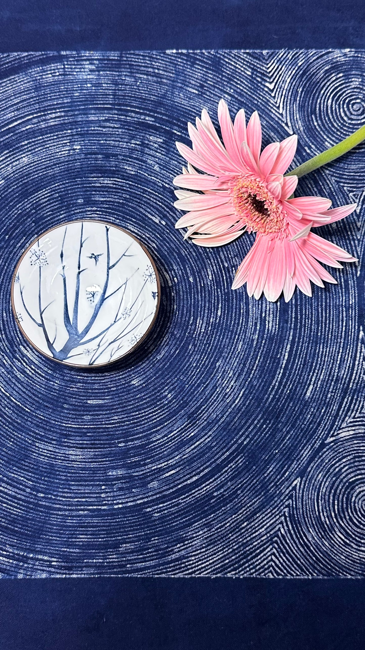 Pink flower on a blue textured surface with a circular object featuring tree branches.