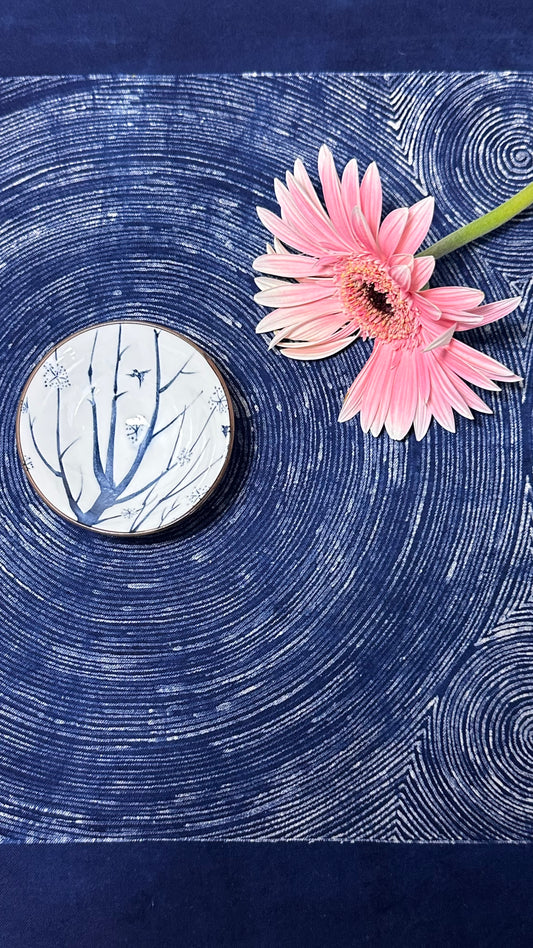 Pink flower on a blue textured surface with a circular object featuring tree branches.