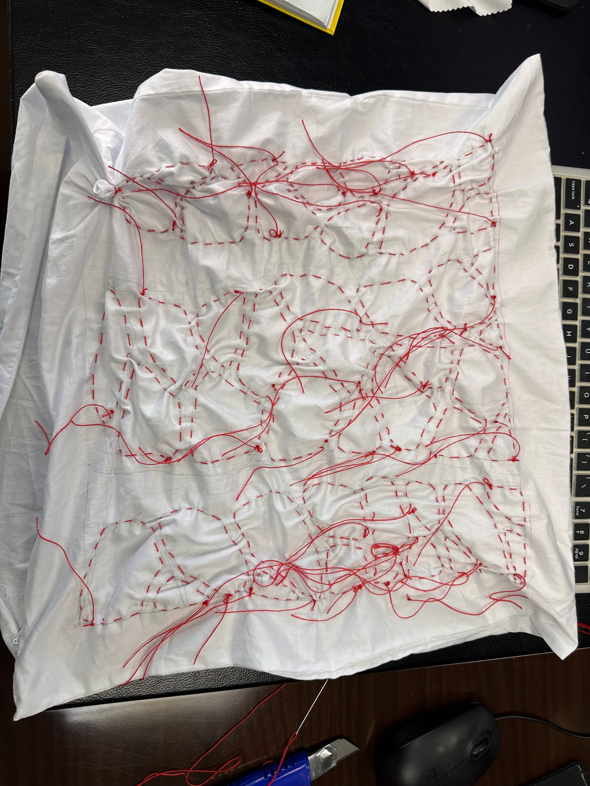 White fabric with red thread patterns on a desk with a laptop and mouse.