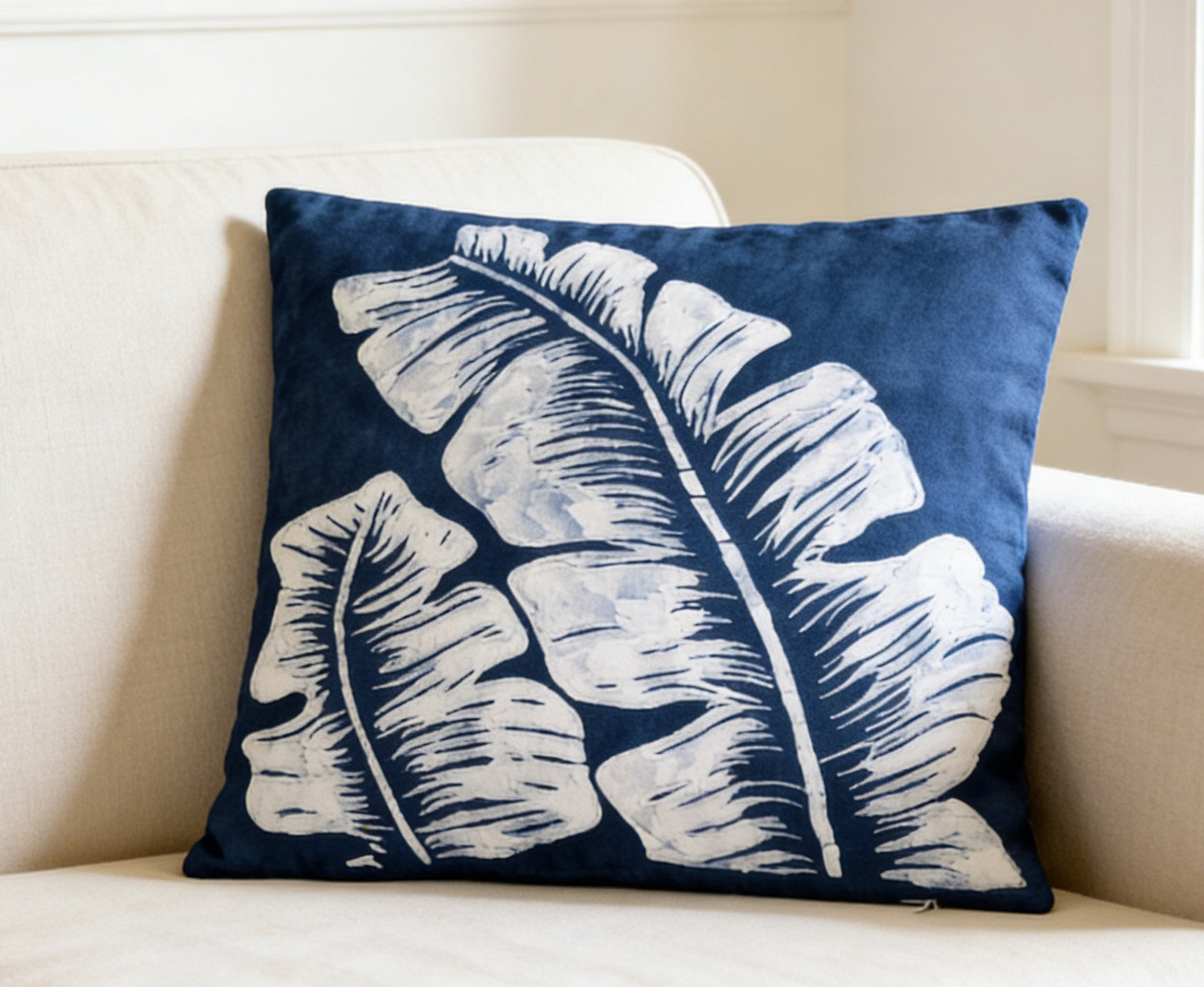 Navy blue pillow with white leaf pattern on a beige couch