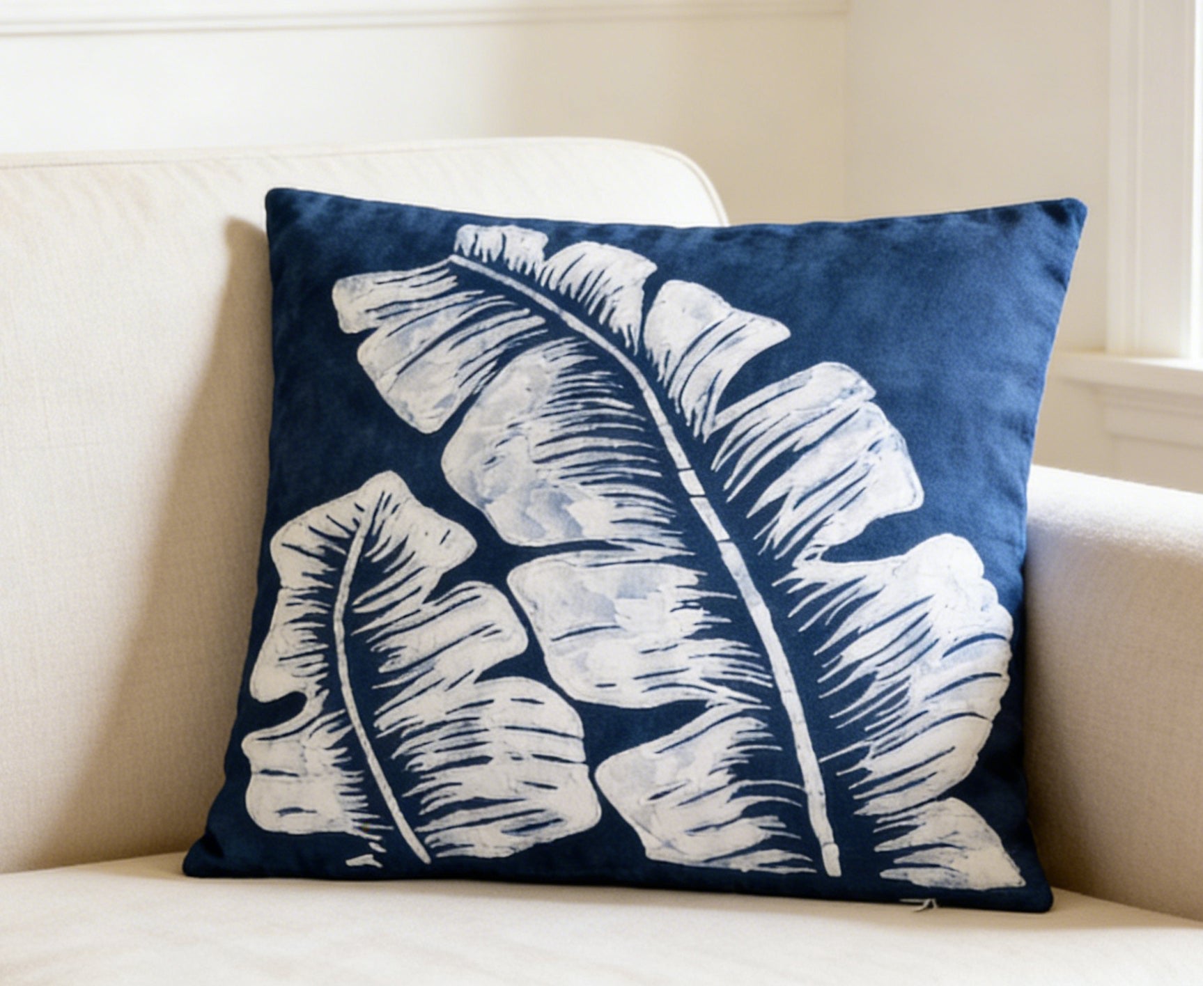 Navy blue pillow with white leaf pattern on a beige couch
