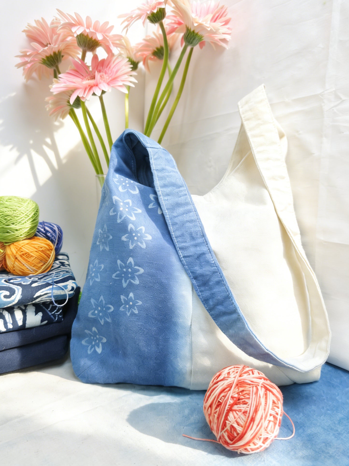 Blue tote bag with floral pattern on a white surface with yarn and flowers.