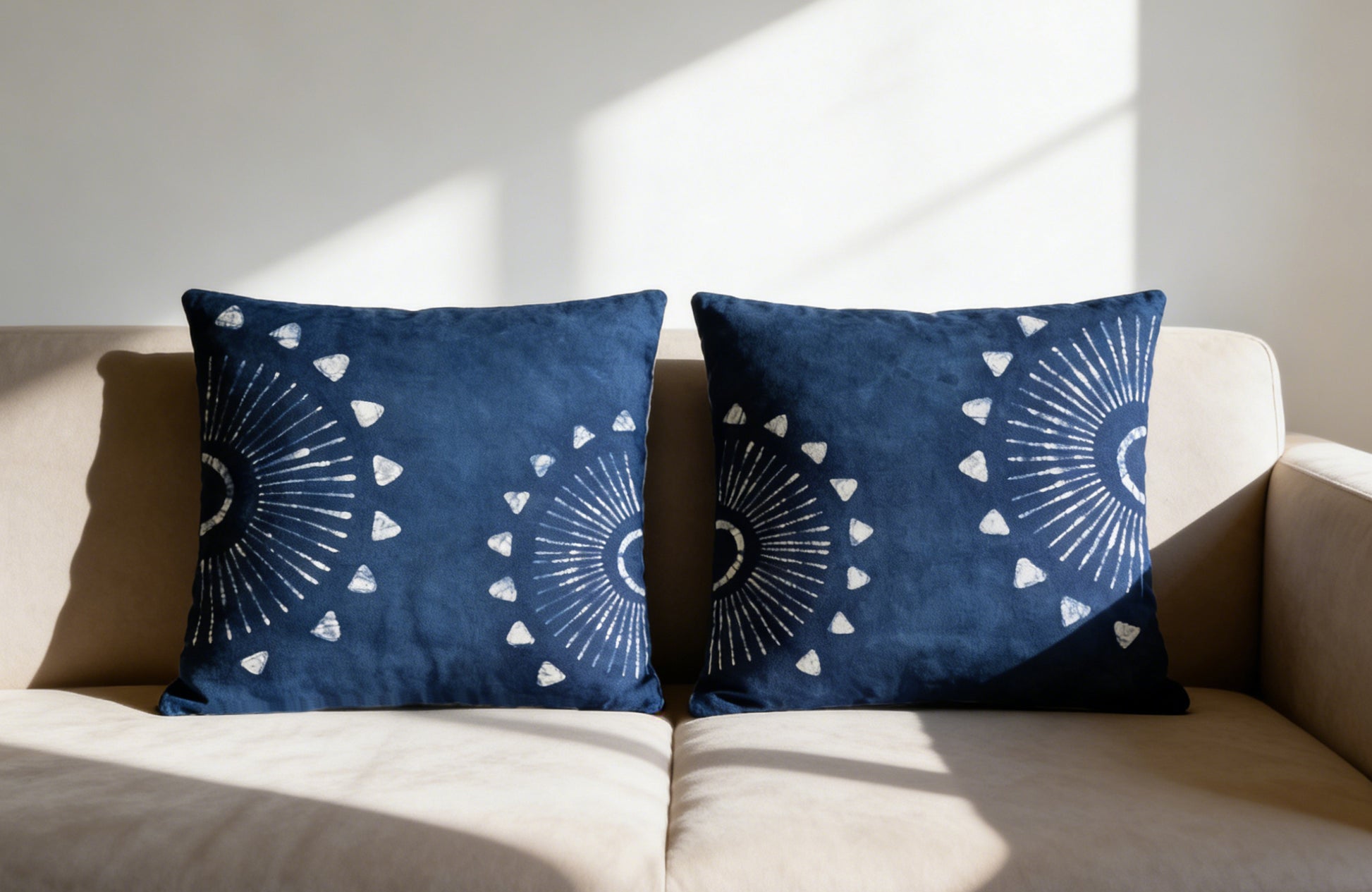 Two blue patterned pillows on a beige sofa with sunlight casting shadows.