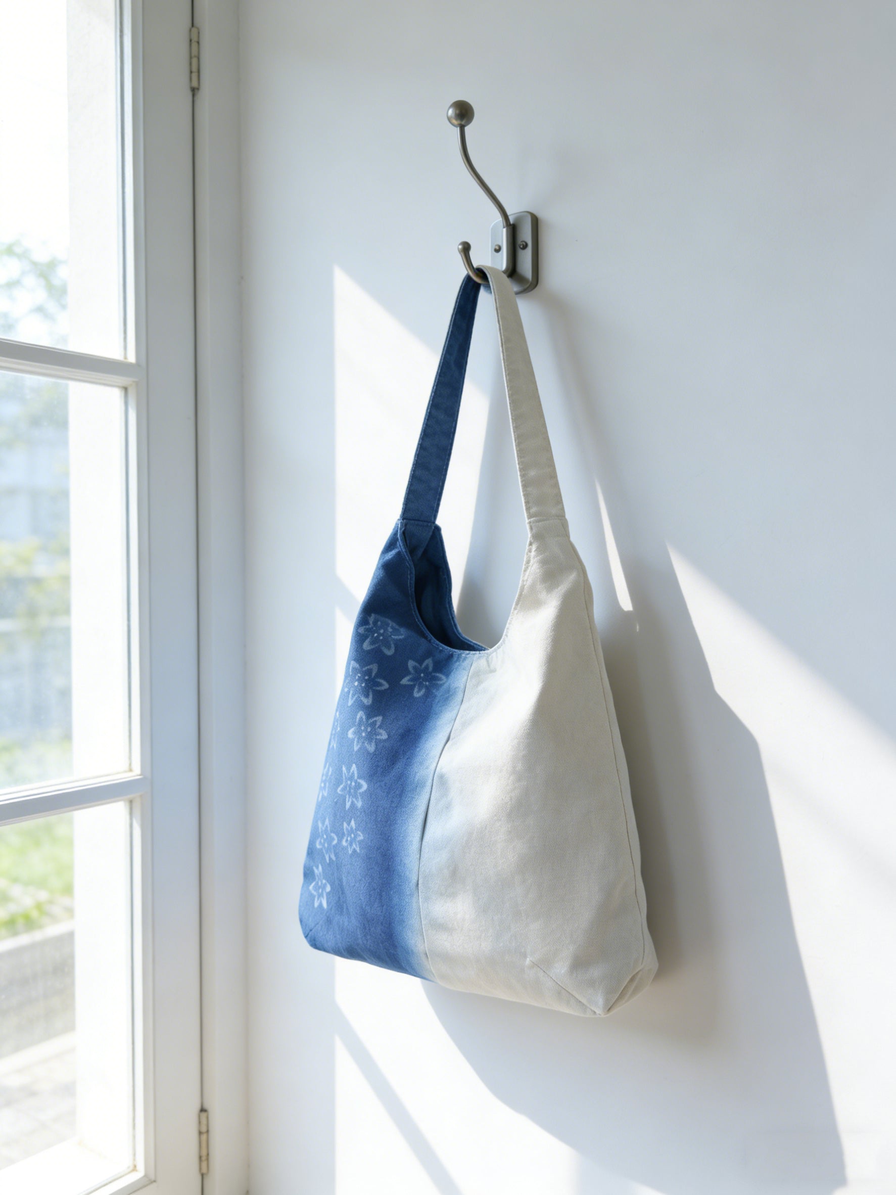 Two tote bags, one blue and one white, hanging on a hook against a white wall.