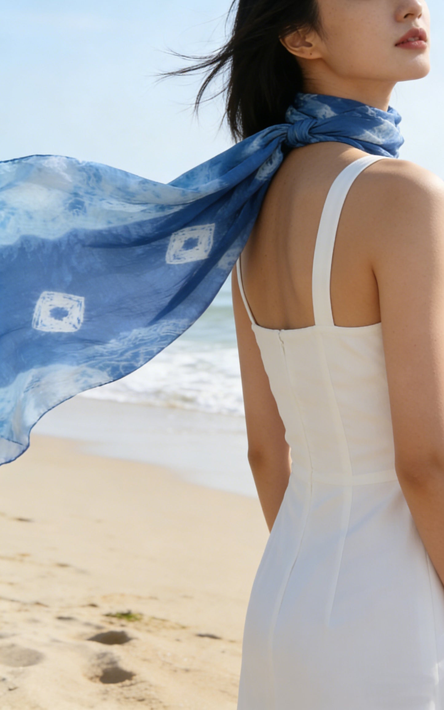 Woman in a white dress with a blue scarf on a beach