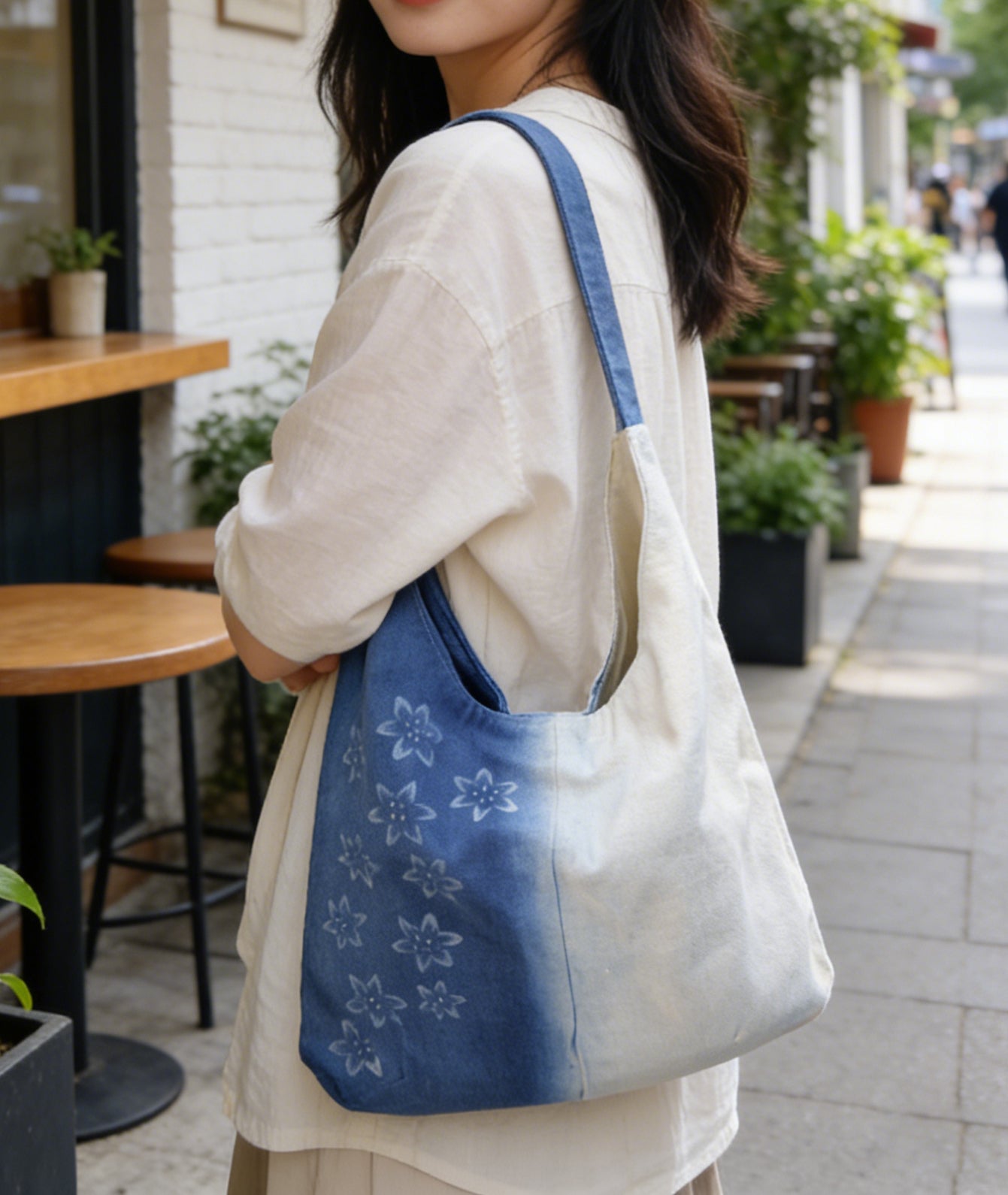 Person holding a blue tote bag with floral patterns in an outdoor setting.