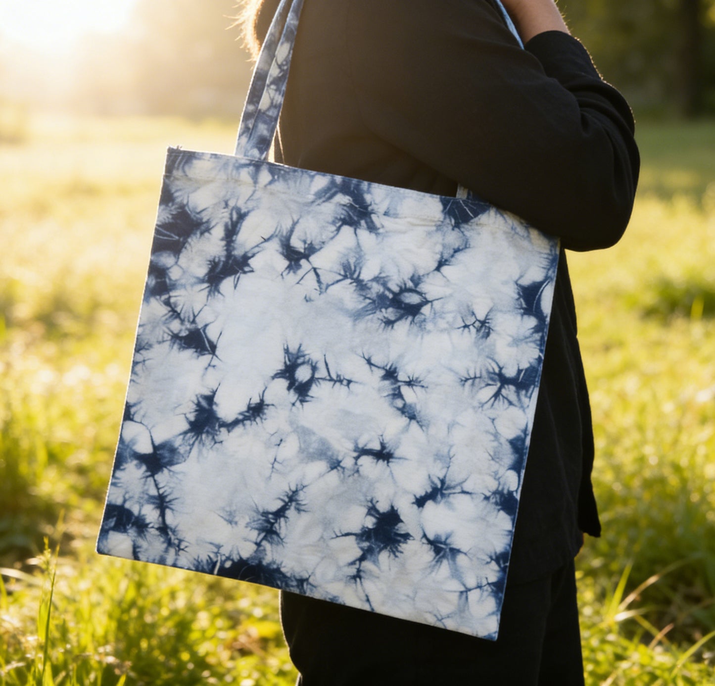 Person holding a tie-dye tote bag in a grassy field
