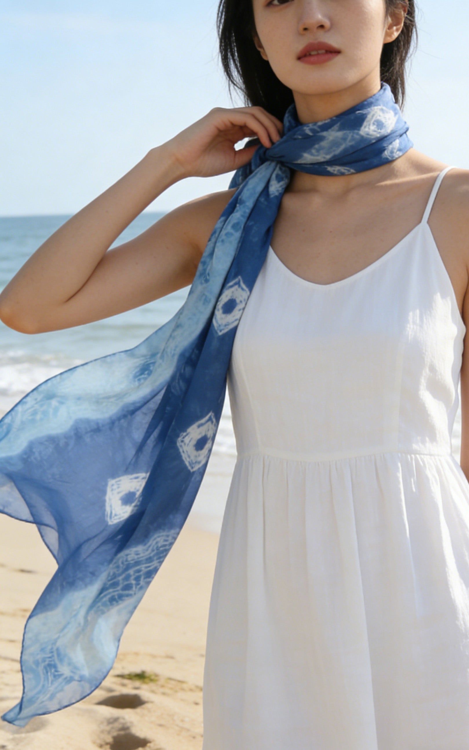 Woman wearing a blue scarf with white patterns on a beach