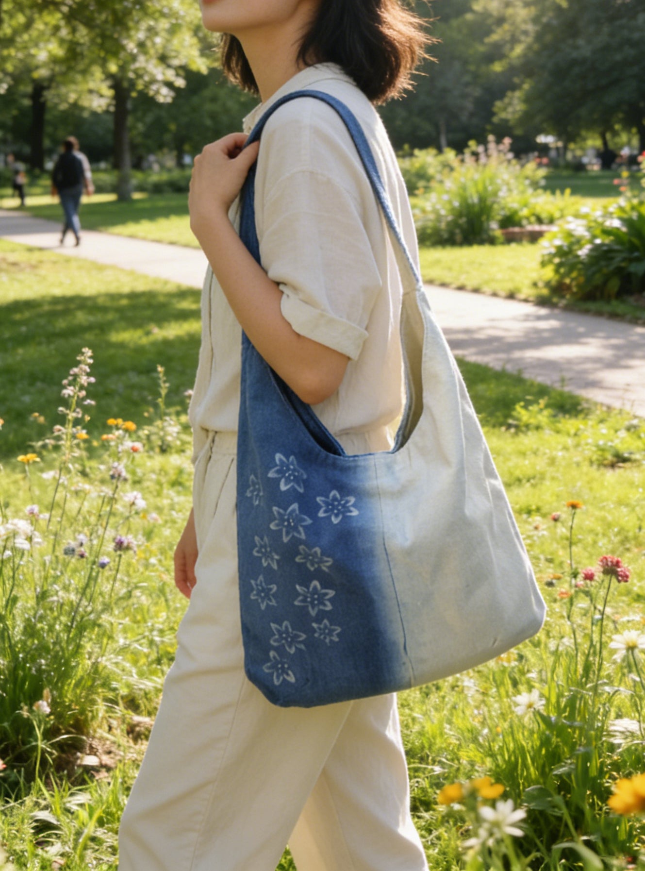 Person holding a blue tote bag with floral patterns in a park setting