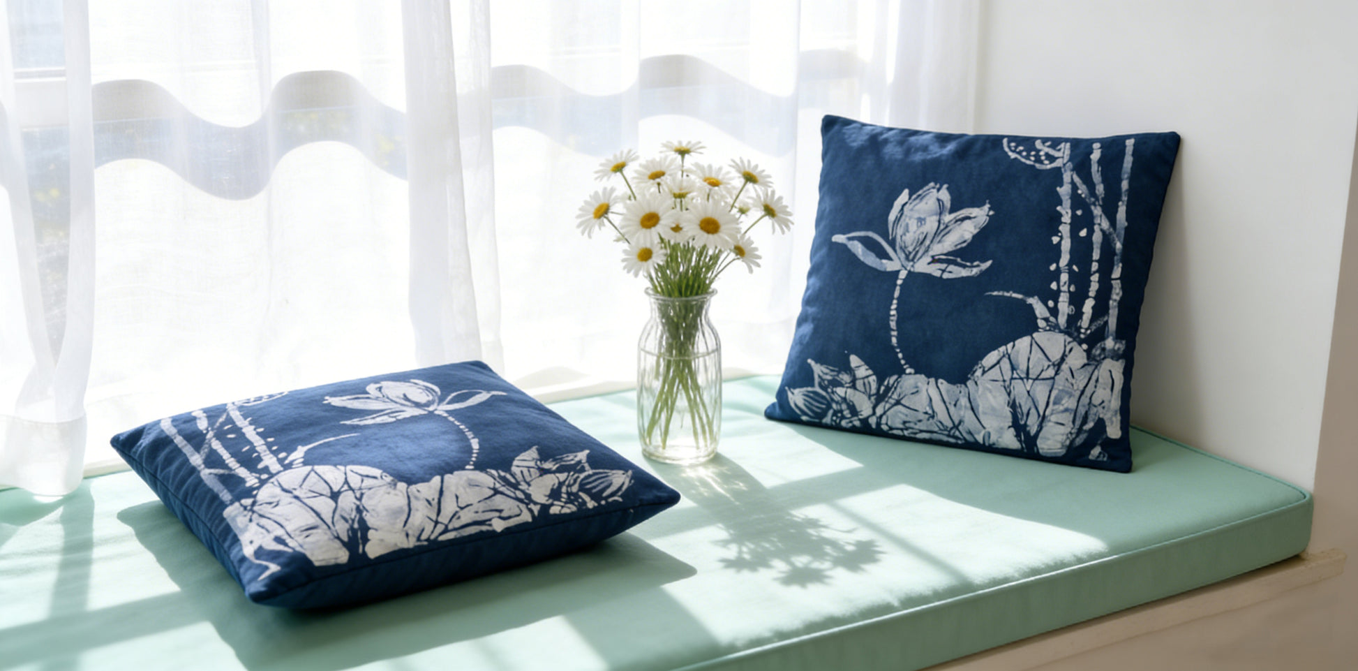 Two blue pillows with white floral patterns on a light green cushion in a bright room.