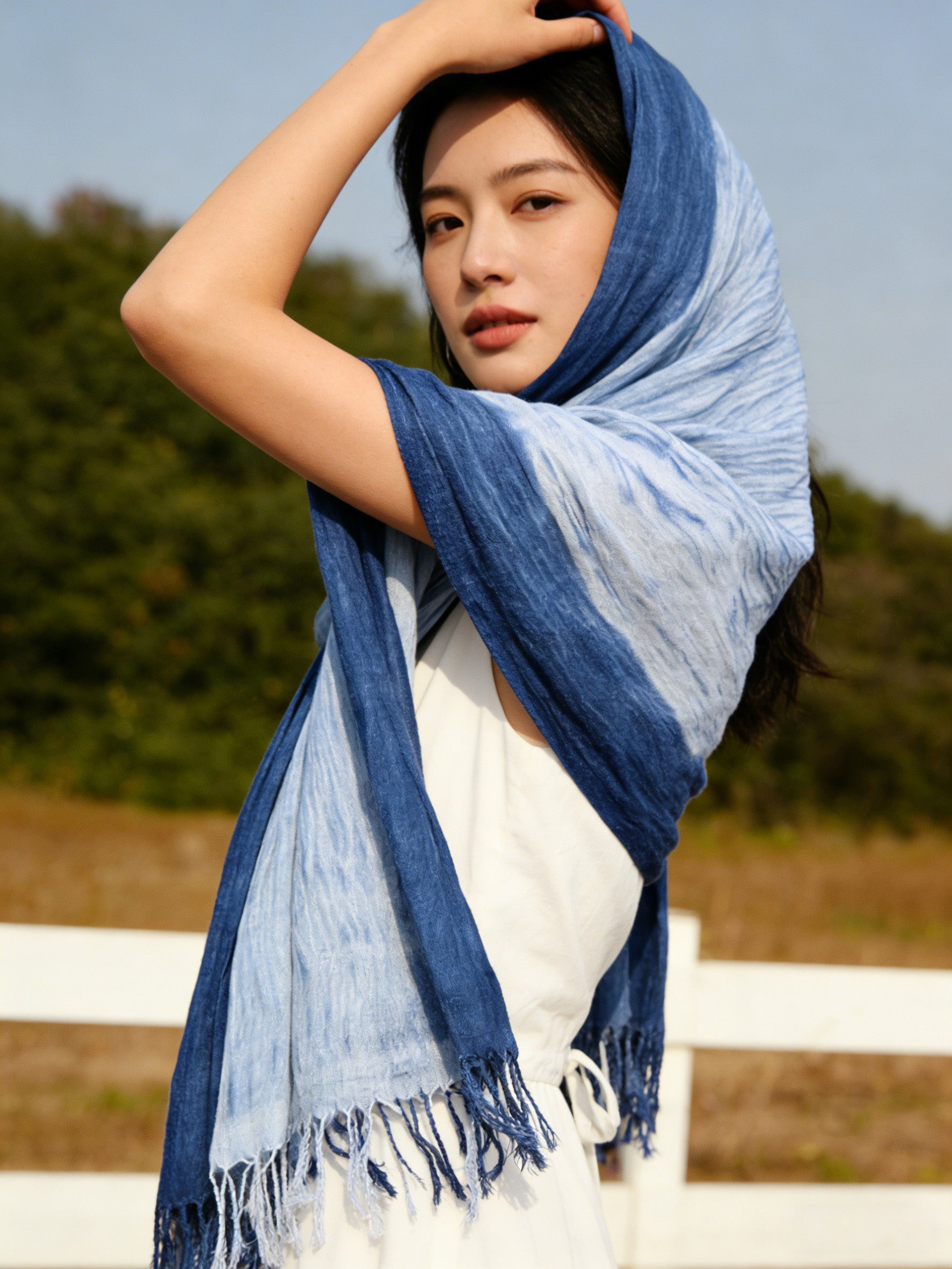 Woman wearing a blue and gray scarf with a blurred outdoor background