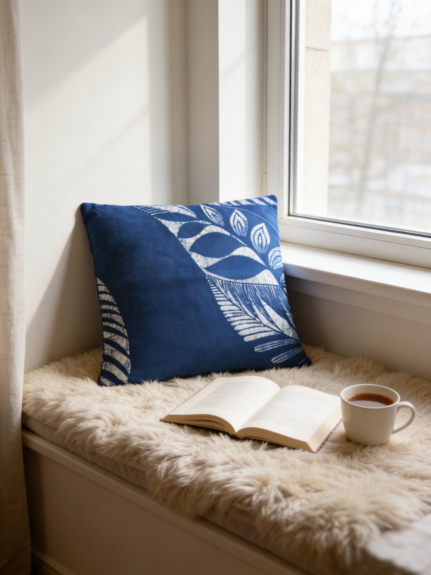 Nook by a window with a blue pillow, open book, and cup of coffee.
