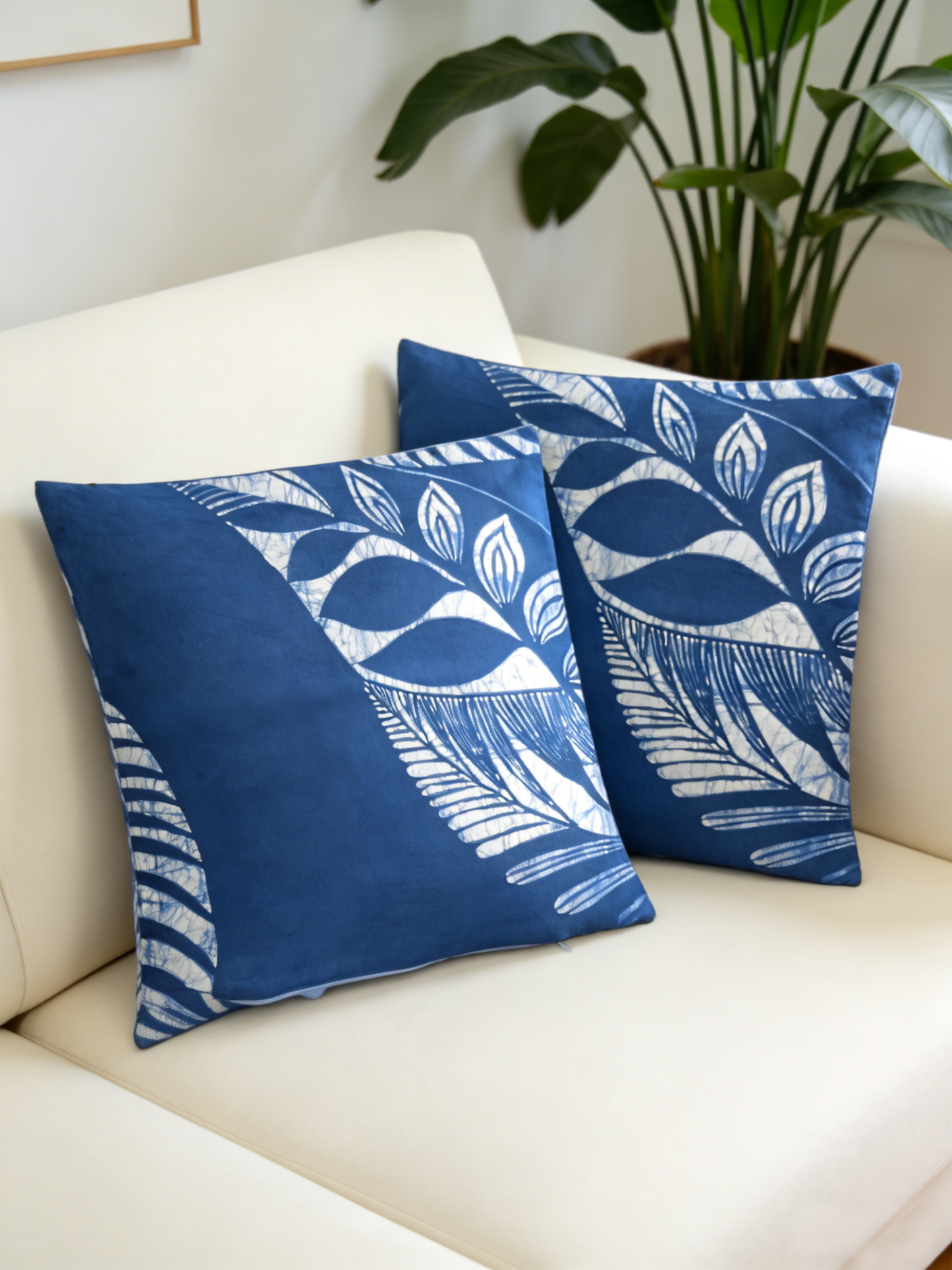 Two blue patterned pillows on a white couch with a plant in the background.