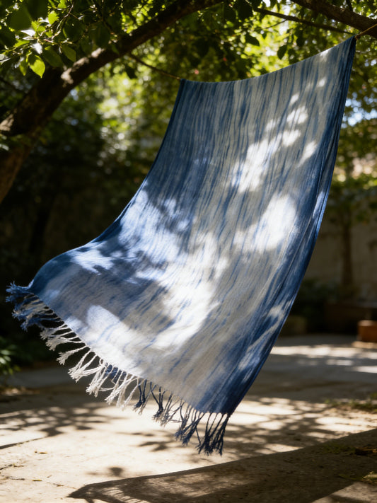 Blue and white striped towel hanging from a tree branch outdoors.