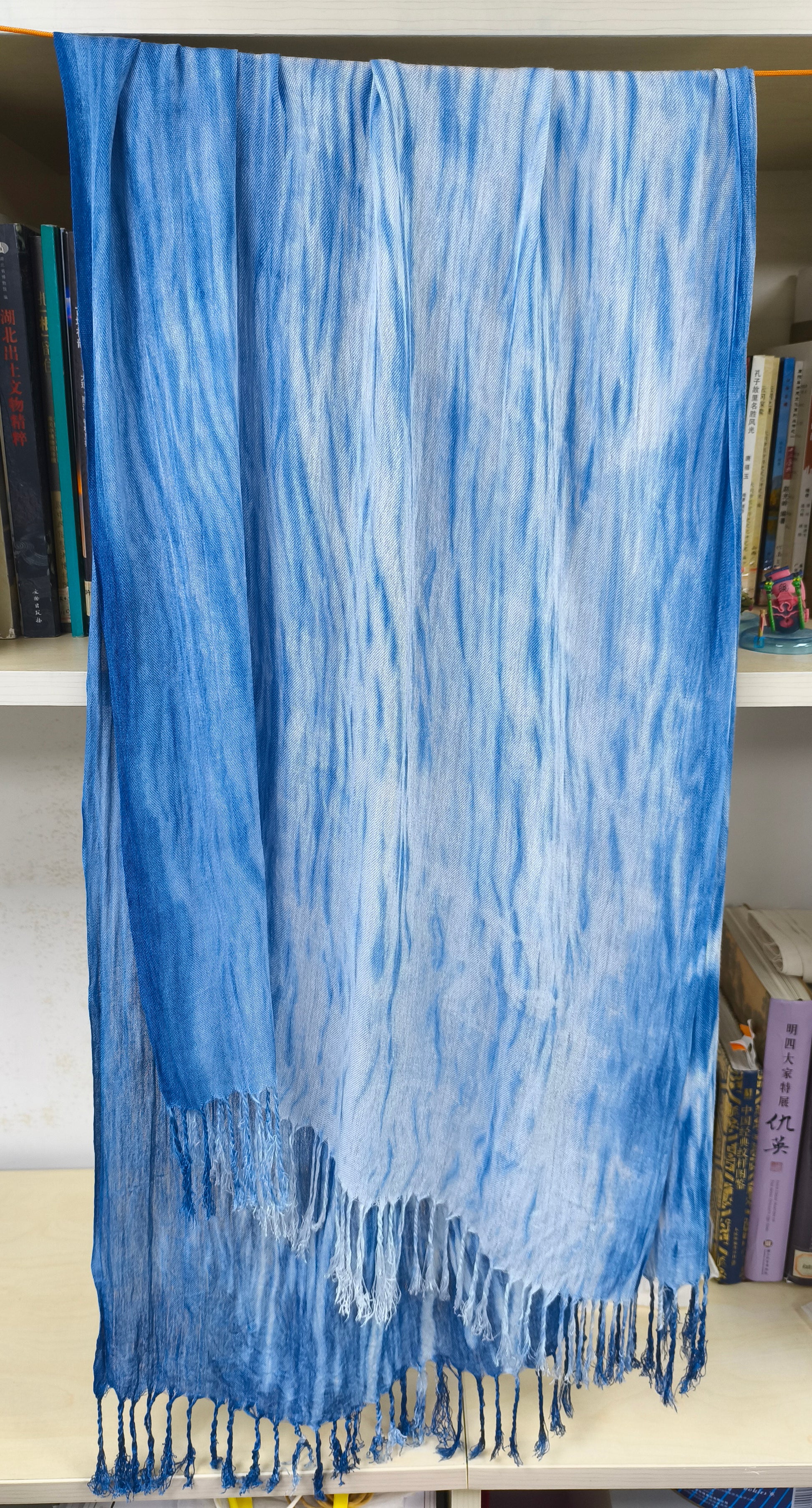 Blue tie-dye scarf with fringes on a white surface